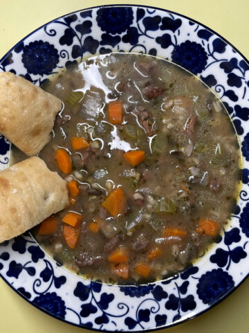 A big bowl of beef and barley soup with two pieces of bread.