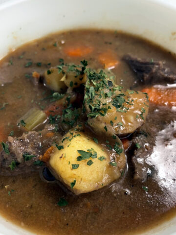 A white bowl filled with rich beef stew. Packed with potatoes and carrots.