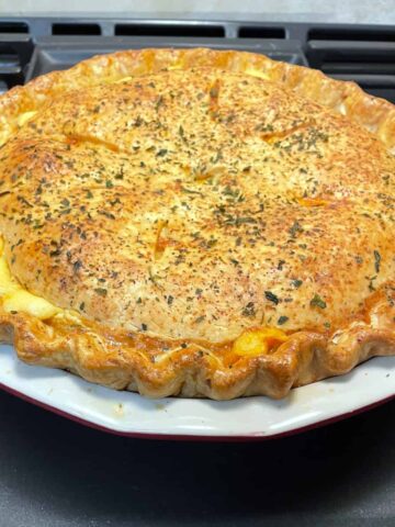 A whole uncut macaroni and cheese pie sits in its white backing dish. The crust is nicely browned and seasoned with cheesy goodness peeking out around the edges.