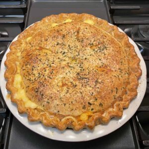 Top down view of a whole uncut macaroni and cheese pie. Displaying its nicely browned and seasoned crust.