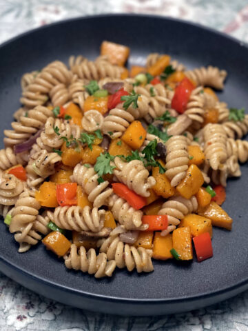 whole wheat fusilli pasta tossed with butternut squash and red peppers served on a stone grey plate.