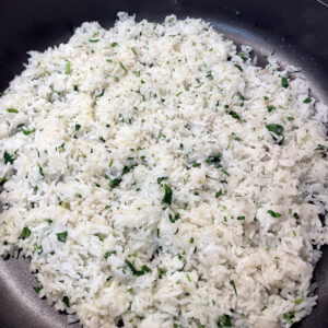 Top down view of a plate full of cilantro lime rice. Grey plate with white rice and specs of green cilantro.