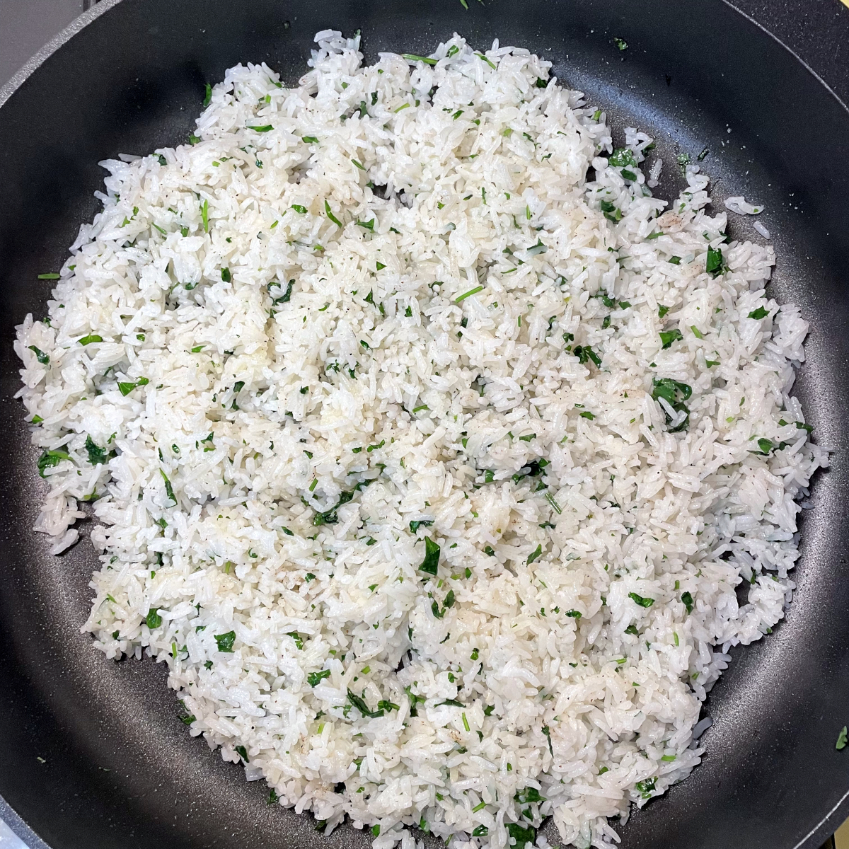 Top down view of a plate full of cilantro lime rice. Grey plate with white rice and specs of green cilantro.