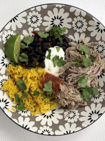 Pulled pork carnitas served along side black beans and yellow rice. Topped with sour cream, cilantro and a lime.