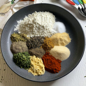 Piles of spices used for making stew mix placed decoratively around a plate. It contains ground mustard, paprika, parsley, cumin, flour and other spices.