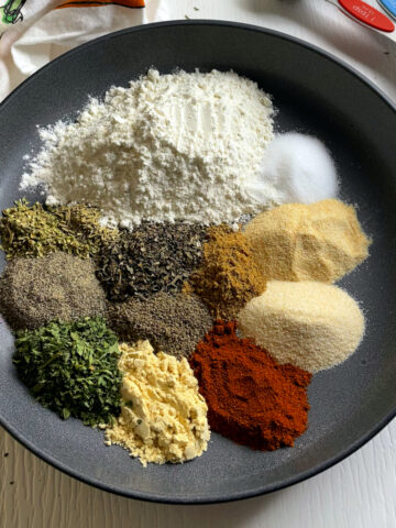 Piles of spices used for making stew mix placed decoratively around a plate. It contains ground mustard, paprika, parsley, cumin, flour and other spices.