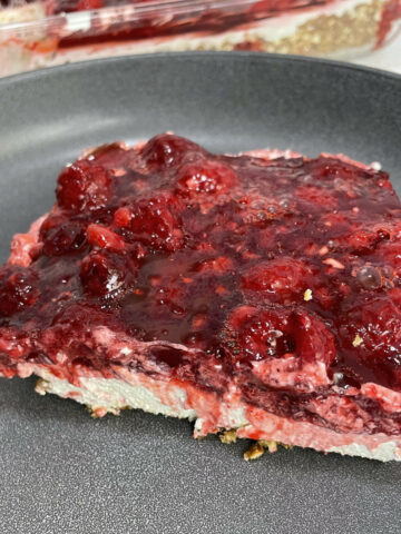 A slice of raspberry jello salad sits on a grey plate.