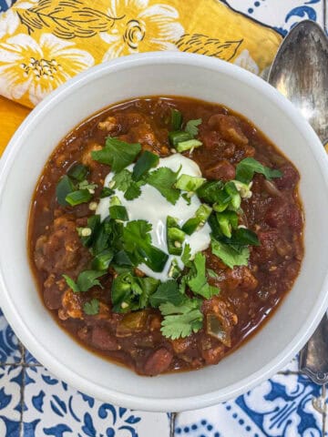 A white bowl filled turkey pumpkin chili topped with sour cream and cilantro