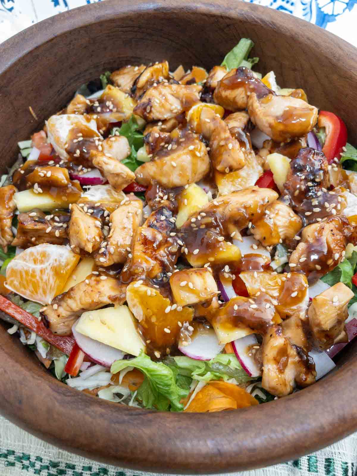 Teriyaki chicken salad served in a teak wood bowl. Tender chuncks of chicken glazed with teriyaki sauce over lettuce peppers and onions.