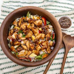 Teriyaki chicken salad served in a teak wood bowl. Tender chuncks of chicken glazed with teriyaki sauce over lettuce peppers and onions.