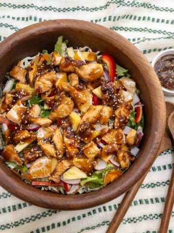 Teriyaki chicken salad served in a teak wood bowl. Tender chuncks of chicken glazed with teriyaki sauce over lettuce peppers and onions.