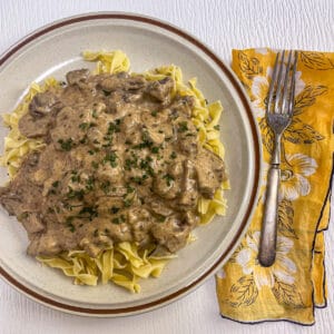 Classic beef stroganoff with egg noodles covered in a creamy beef and mushroom sauce topped with sprinkled parsley.