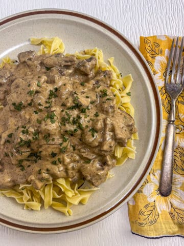 Classic beef stroganoff with egg noodles covered in a creamy beef and mushroom sauce topped with sprinkled parsley.